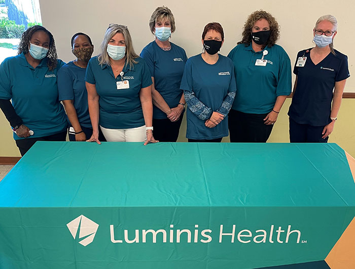 masked health workers stand behind a table bearing the Luminis Health logo