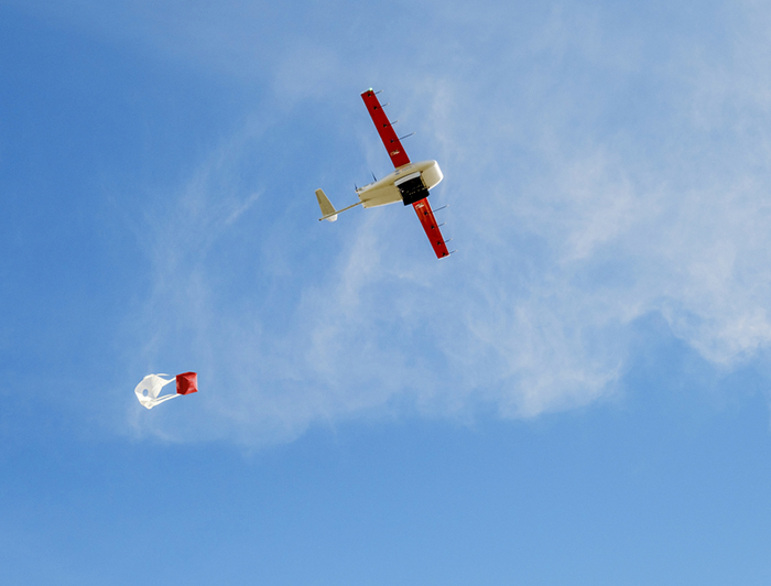 Zipline drone flies across blue sky trailing a package for delivery