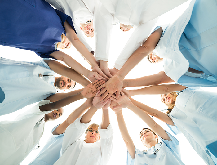 Diverse medical team stacks hands in team huddle shot from below