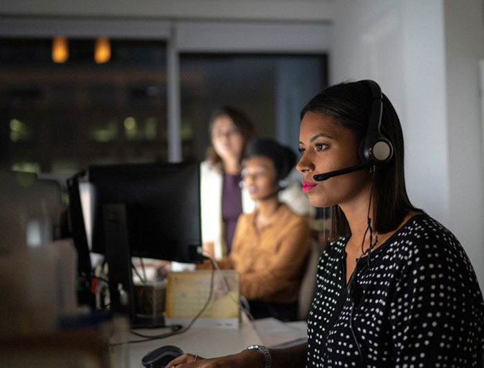 Profile of a woman with a communications headset on with others in the background