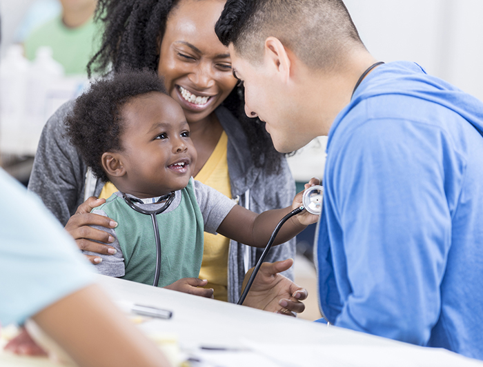 mother and doctor smile while baby plays with stethoscope
