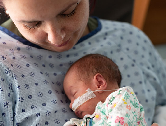 Norton Children's Hospital. Stock photo of new mother in hospital gown holding tiny baby
