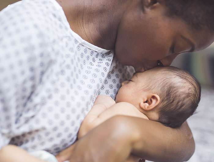 Dartmouth Health. A new mother in hospital gown kisses her newborn
