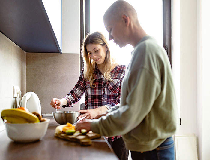 Bald female cancer patient working with a nutritionist to prepare a healthy dish