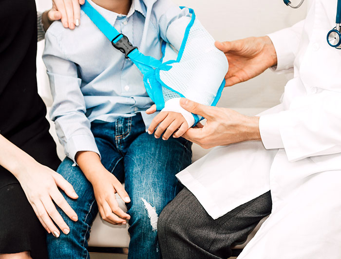Nemours Childrens. A child wearing a sling sits being examined by a doctor