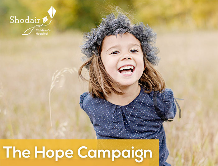 Shodair Children's Hope Campaign ad features a young girl smiling in a field of tall grass