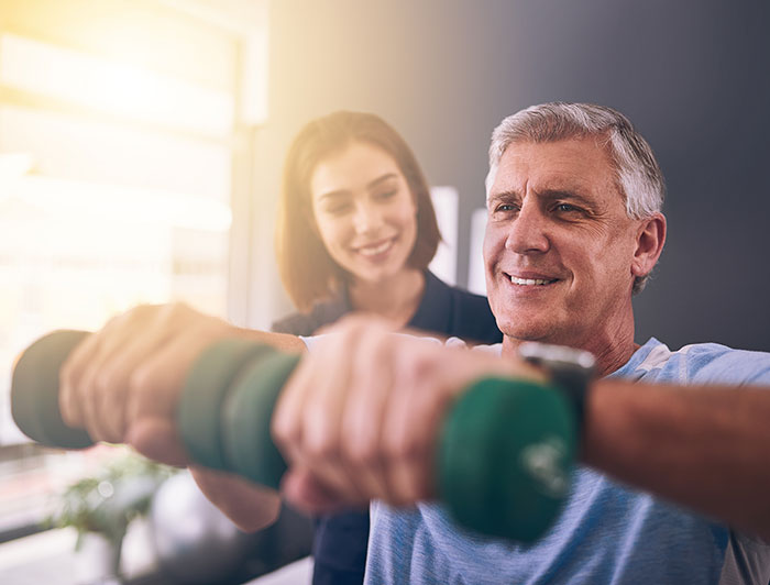 Kent Hospital’s Spaulding Rehabilitation teams offer life-changing health care to patients of all ages - image of young female physical therapist working with a middle aged man who is holding light dumbells