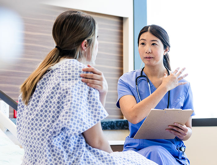 St. Joseph Hospital. A female nurse in scrubs talks with a female patient sitting in a hospital bed