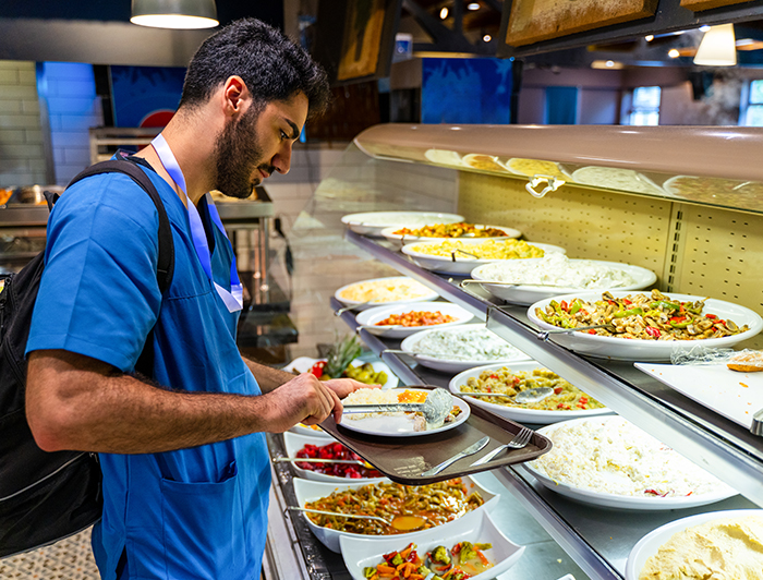 Maine Health. A male health worker in scrubs stands at a buffet preparing a plate of food