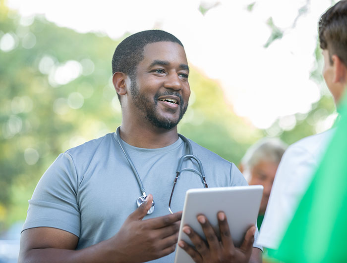 St. Francis Hospital. A health worker holding a tablet speaks with a patient at an outdoors community event