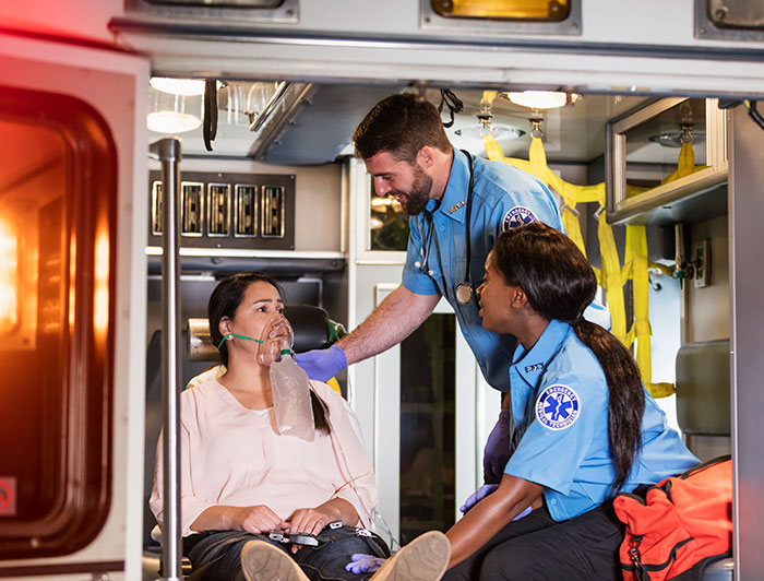 CommonSpirit Mercy Hospital. stock image of a EMTs administering oxygen to a woman sitting on a stretcher