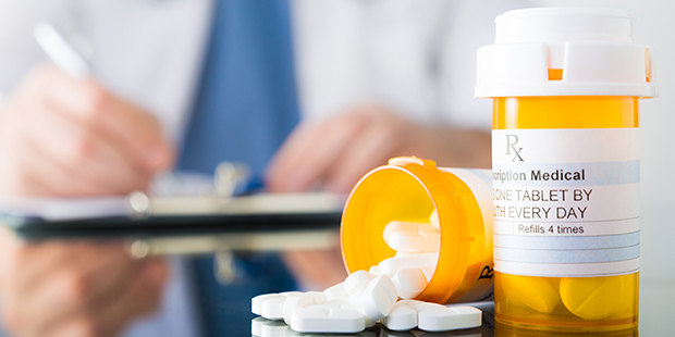 Physician writing prescription in background with pill bottles and medication in foreground