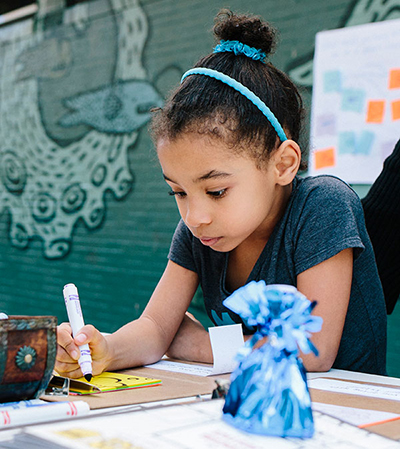 girl at table outside drawing with a marker
