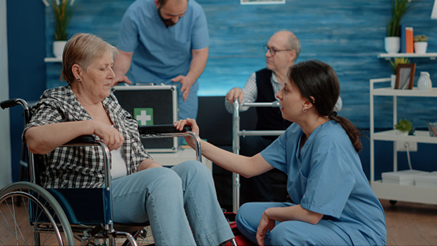 5 Innovative Nurse-Led Models of Care to Explore. A crouching nurse speaks to a patient who is sitting in a wheelchair.