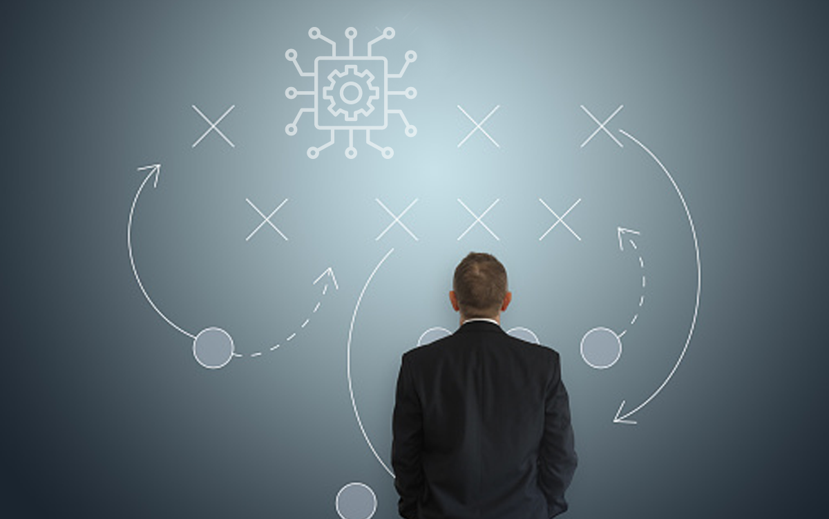 AI Certification Program, Best-Practices Tools Coming This Fall. A businessman stands looking at a chalkboard on which there is an AI icon and plays drawn up.