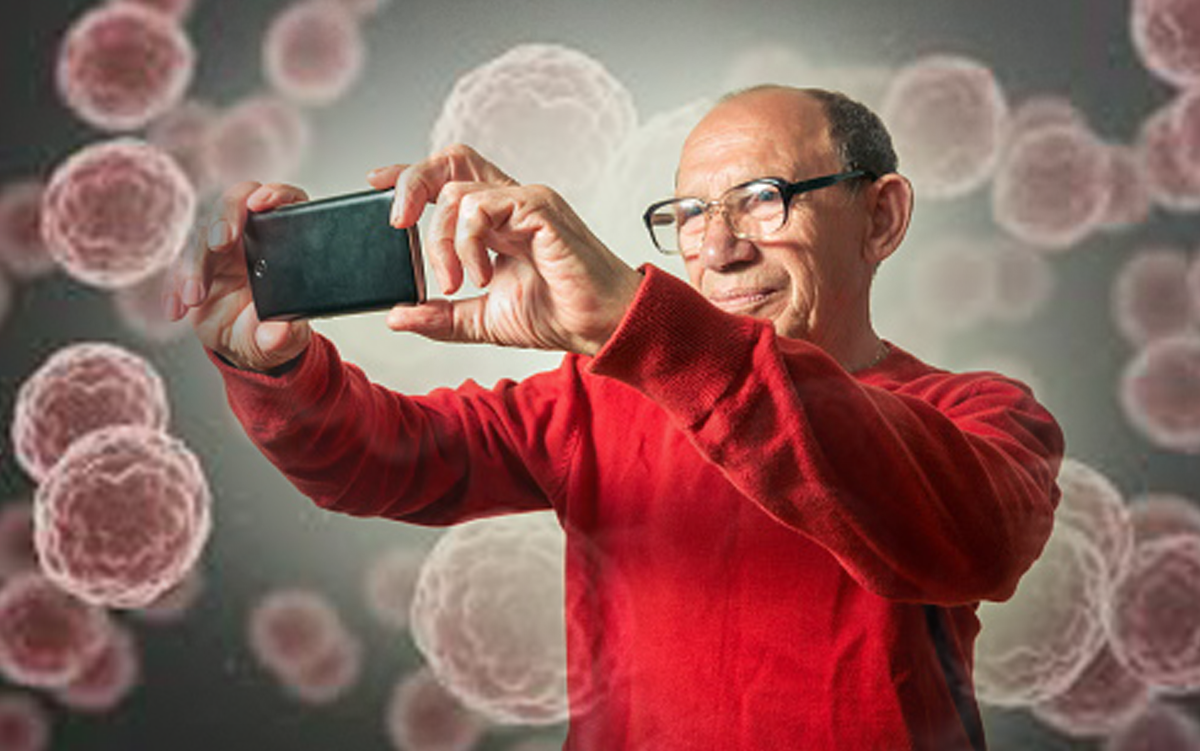 Can a Selfie Really Estimate One's Age and Predict Cancer Outcomes? A man standing in front of a background of cancer cells holds up his mobile phone and takes a selfie of himself.