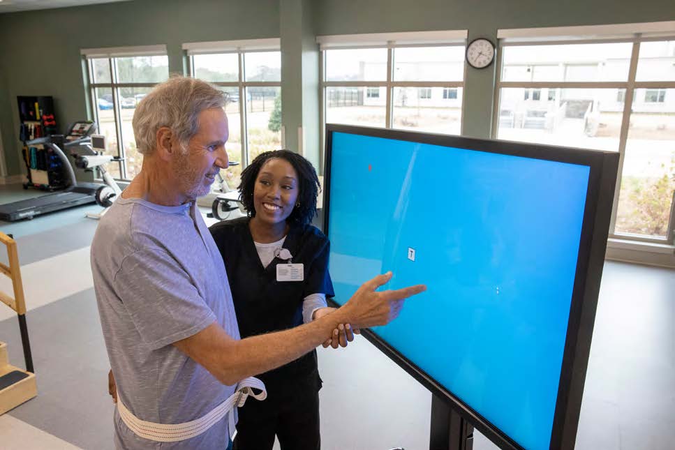 Billy, a volunteer firefighter who suffered a stroke while responding to an emergency call, touches a large screen with the help of a therapist at The Rehabilitation Institute of Southern Illinois, a partnership of BJC HealthCare and Encompass Health.