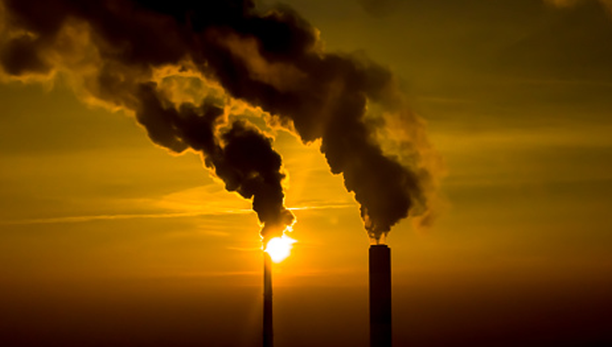 AHA Market Scan Takeda and Boston Medical Center Partner to Cut Health Care Emissions. Two smokestacks billowing smoke with a smoggy sunset in the background.