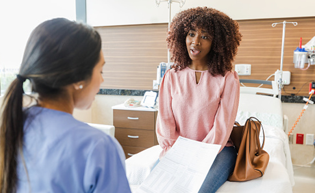 Women’s Health Startup Tia Makes an Impact Treating ‘Medical Orphans’. A Black woman sitting on an examination table talks with her doctor.