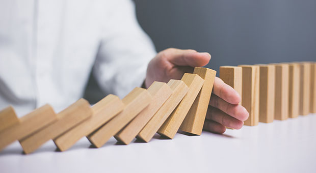 How to Hinder Innovation stock image of hand stopping dominoes from falling