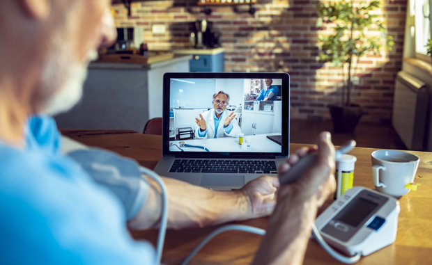 Studies Find That Remote Monitoring Advanced Care During Pandemic. A patient checks his blood pressure while speaking to a doctor on his laptop computer using remote patient monitoring (RPM) technology.