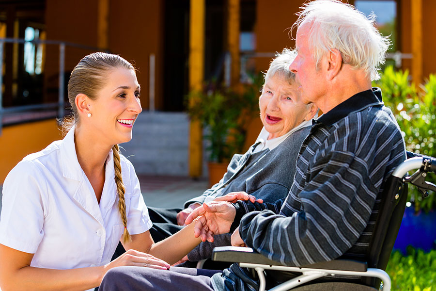 CAPC A nurse speaks with an elderly couple outdoors at a rehab facility.