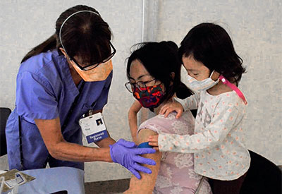 Mother receives vaccination from Huntington worker while toddler looks on