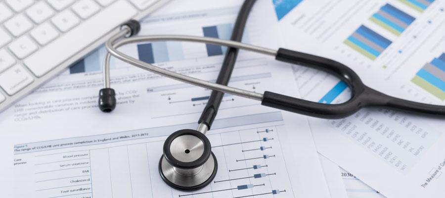 A stethoscope and a keyboard sit sit on data tables and charts