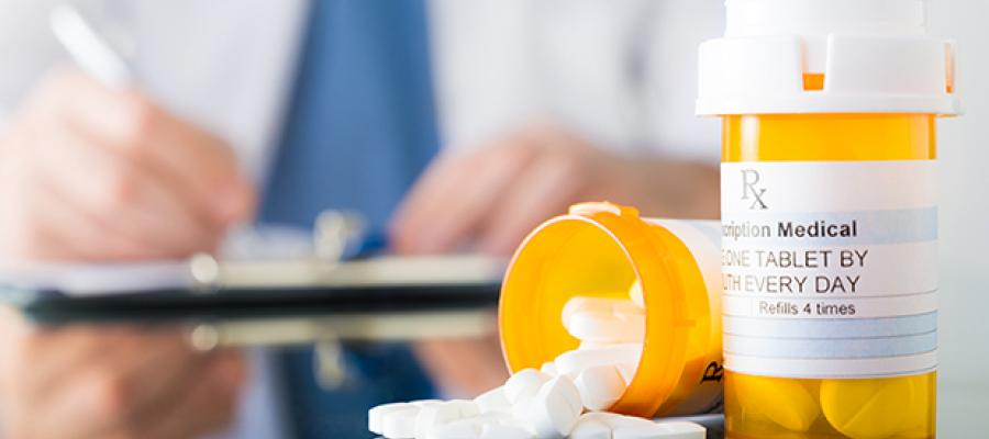 Physician writing prescription in background with pill bottles and medication in foreground
