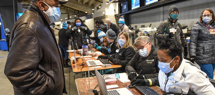 Older Black man wearing medical mask checks in at stadium with health workers seated at tables