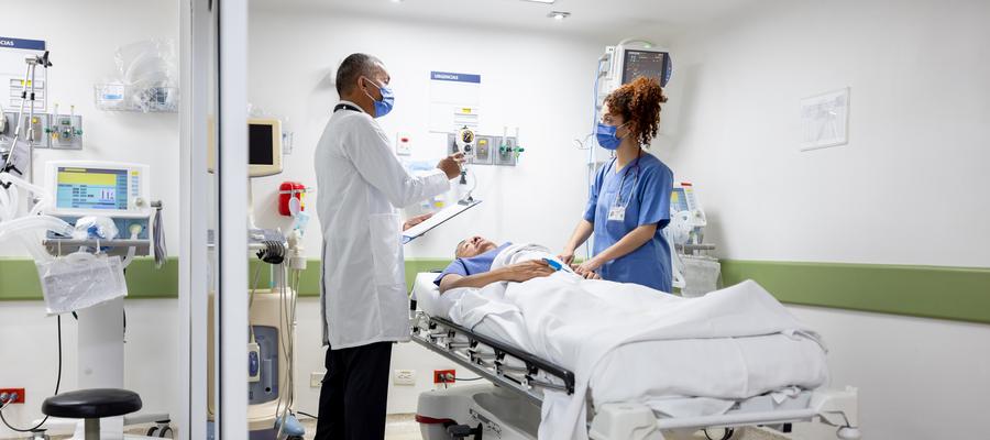 Two health care workers treat a patient laying in a hospital bed.