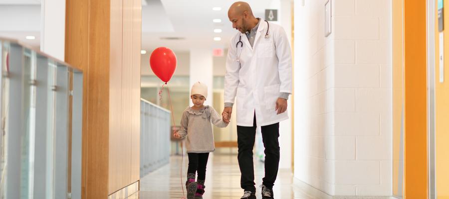 A child walks down a hospital holding the hand of a health care provider.
