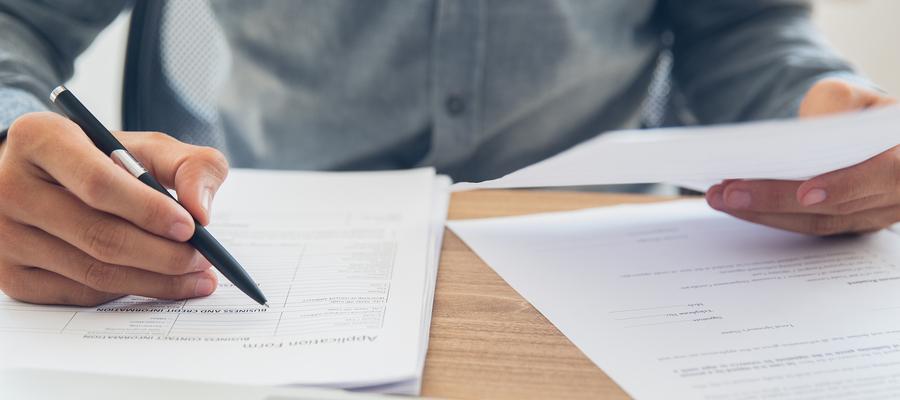Man's hands hold a pen while he looks at forms
