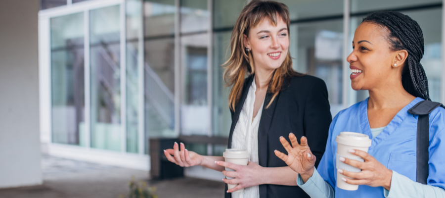 Two women holding coffee cups take a walk outside hospital 