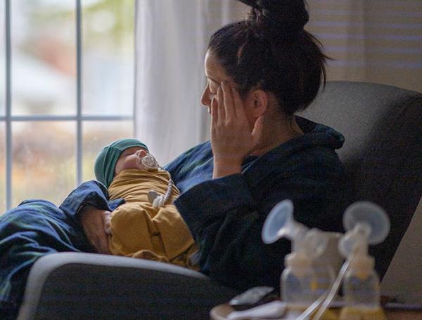 Stock photo of a new mother sitting in a rocking chair with an infant, breast pump bottles in foreground