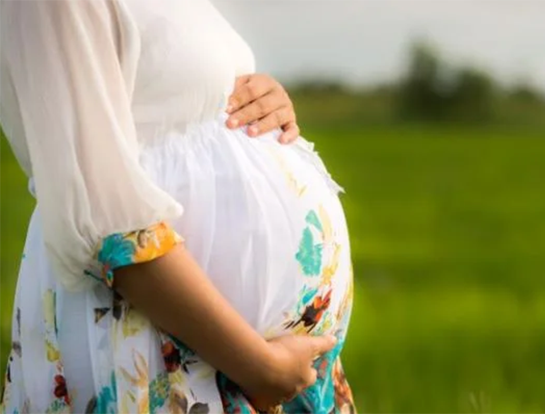 A mother wearing white dress cradles her pregnant stomach