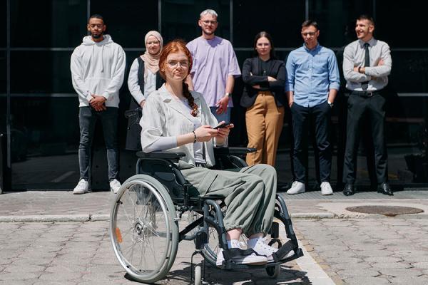 Addressing Health Disparities. A women in a wheelchair in front of a diverse group of men and women.