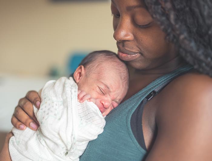 A Black mother sits holding her newborn baby