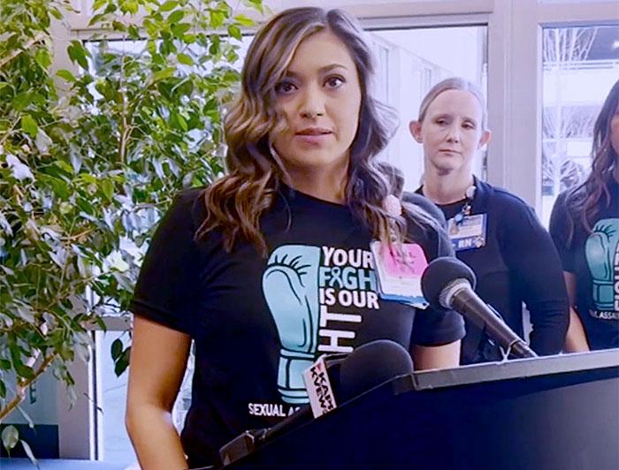 Woman stands at podium wearing a tee that reads "Your Fight is our Fight"