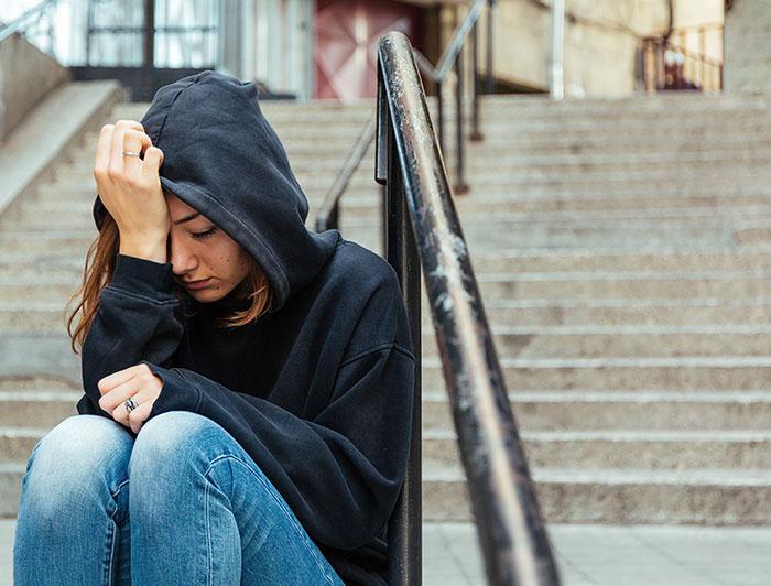 Stock image of a teen girl sitting on steps, hoodie pulled up, looking sad or upset