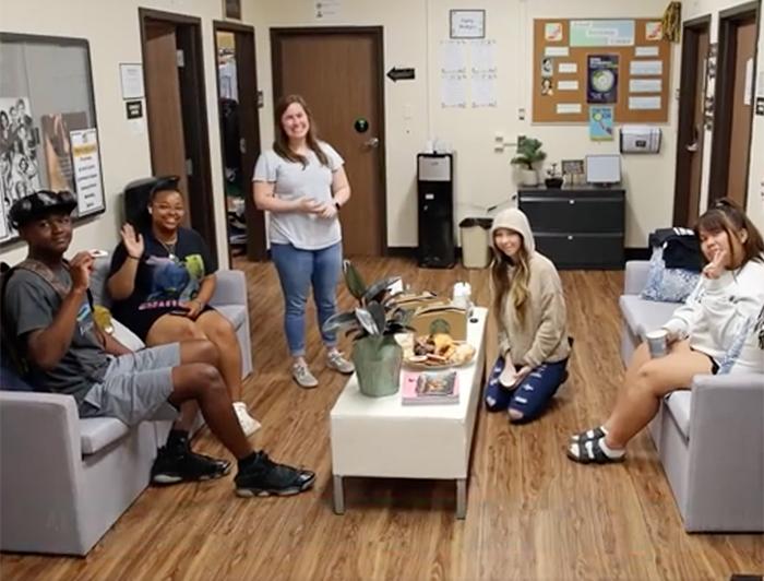 Five diverse smiling teens sit in a school office