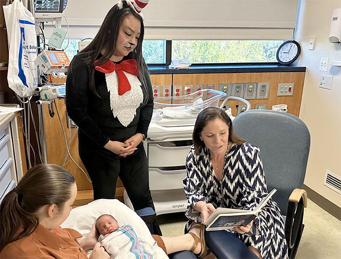 FirstHealth Moore Regional Hospital. A nurse dressed up like the Cat in the Hat looks on as a woman reads a book to a newborn infant held by its mother.