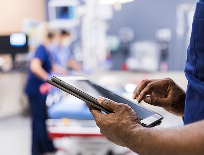 stock photo shows hands of a health worker in scrubs holding a tablet computer