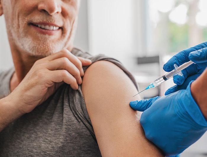 Wallowa Memorial Hospital. An older man sits smiling while gloved hands administer vaccine in his arm