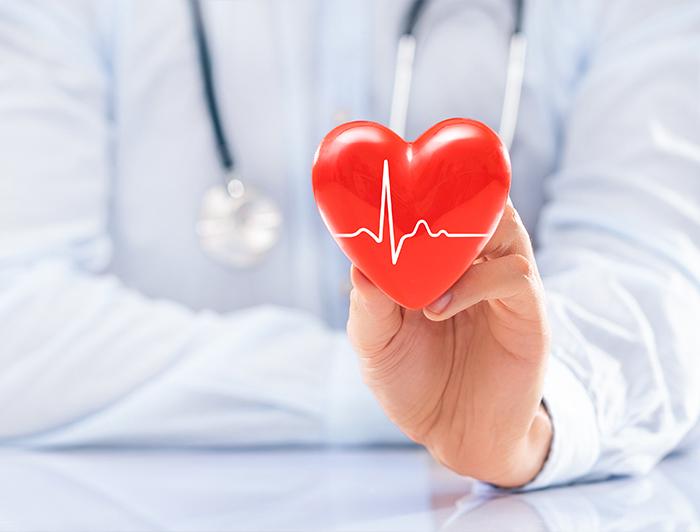 Stock image of a faceless clinician in white coat and stethoscope holding a up a plastic heart shape
