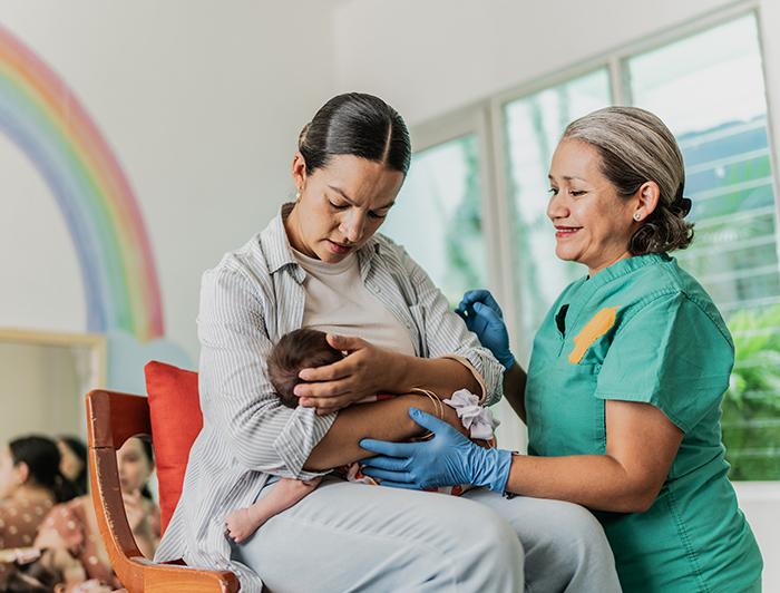 A nurse midwife in scrubs helps a woman attend to her infant