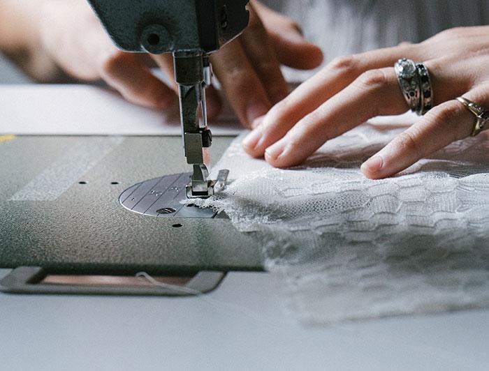 Close-up of hands guiding wedding dress fabric through a sewing machine