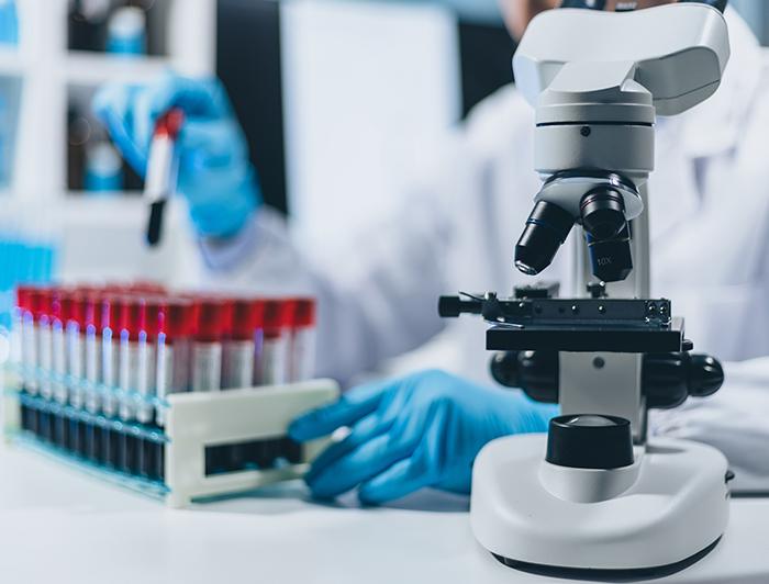 Stock image of a lab scientist sitting behind a microscope holding a test tube