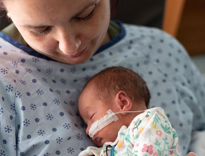 stock image of a mother in hospital gown cradling tiny baby