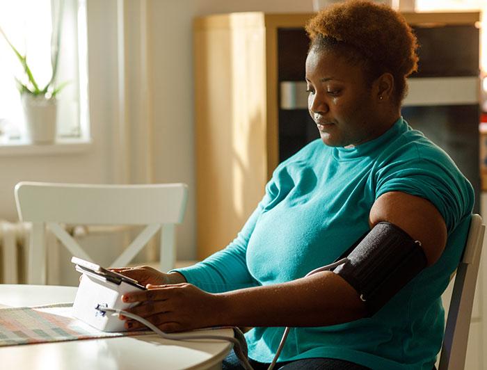 A woman sits at a kitchen table using a home bp monitor